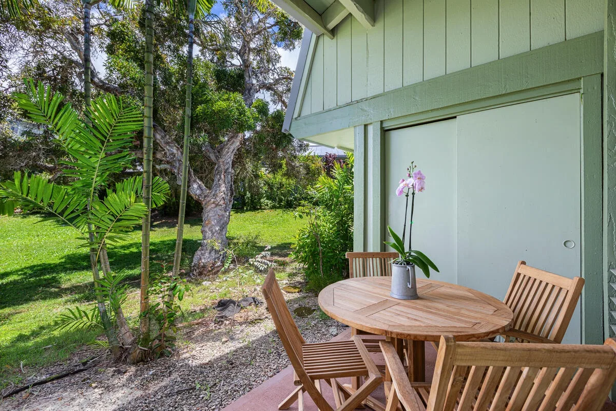 Un patio exterior con una mesa redonda de madera y sillas junto a un jardín.