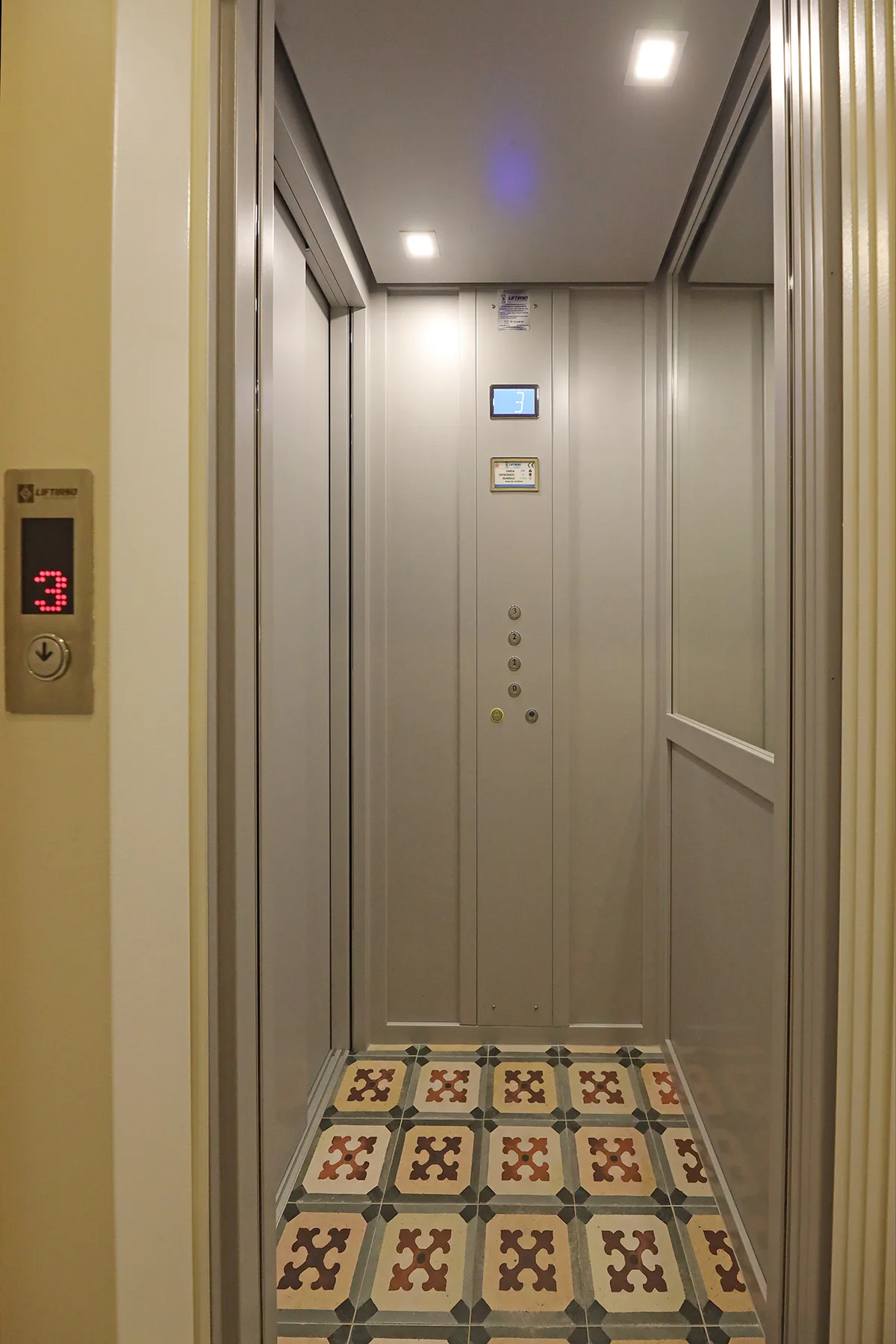An elevator interior with patterned tile flooring and a control panel.