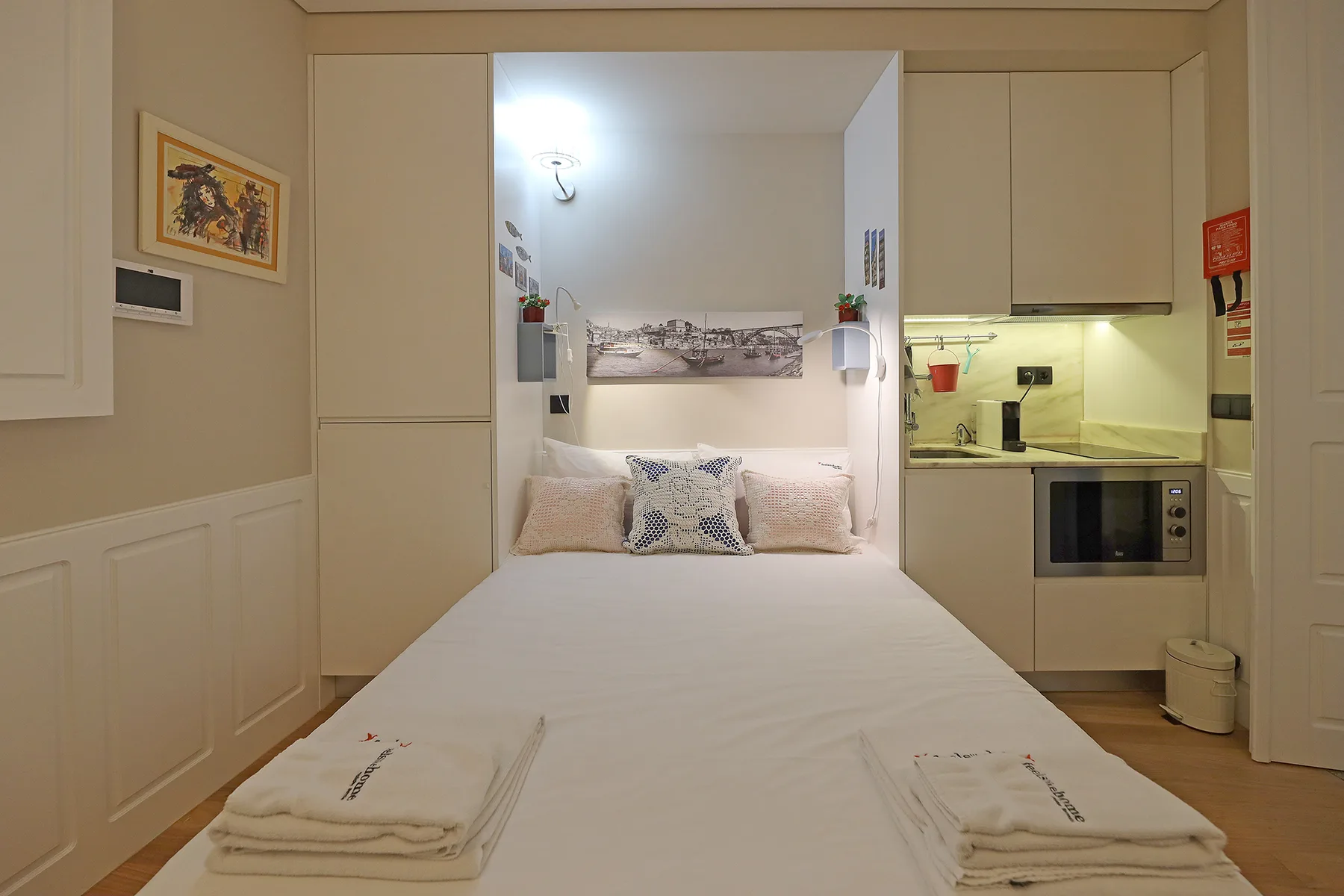 A bedroom with a neatly made bed and a compact kitchenette.