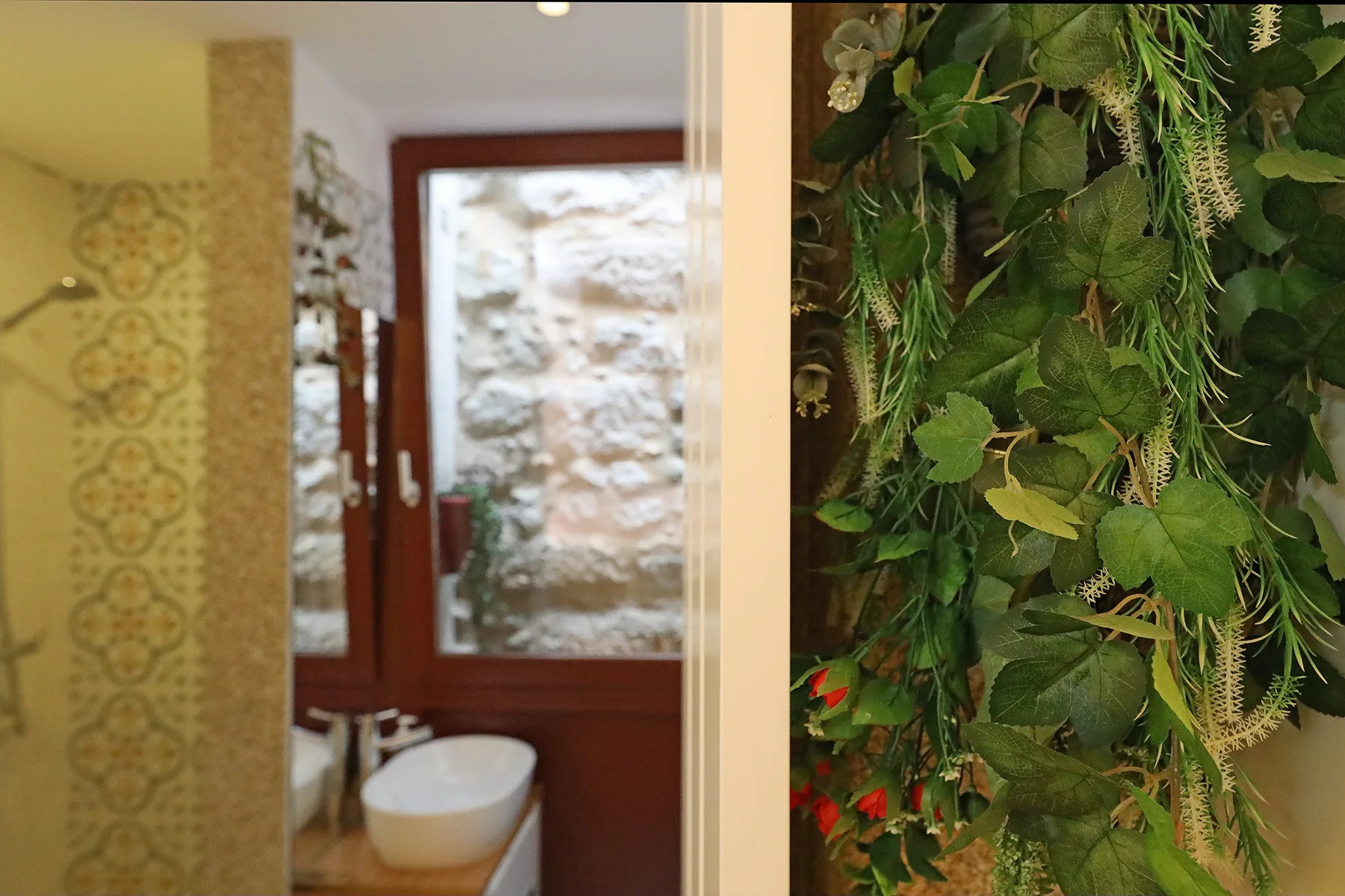 A bathroom with patterned wall tiles, a sink, and leafy plants beside the doorway.
