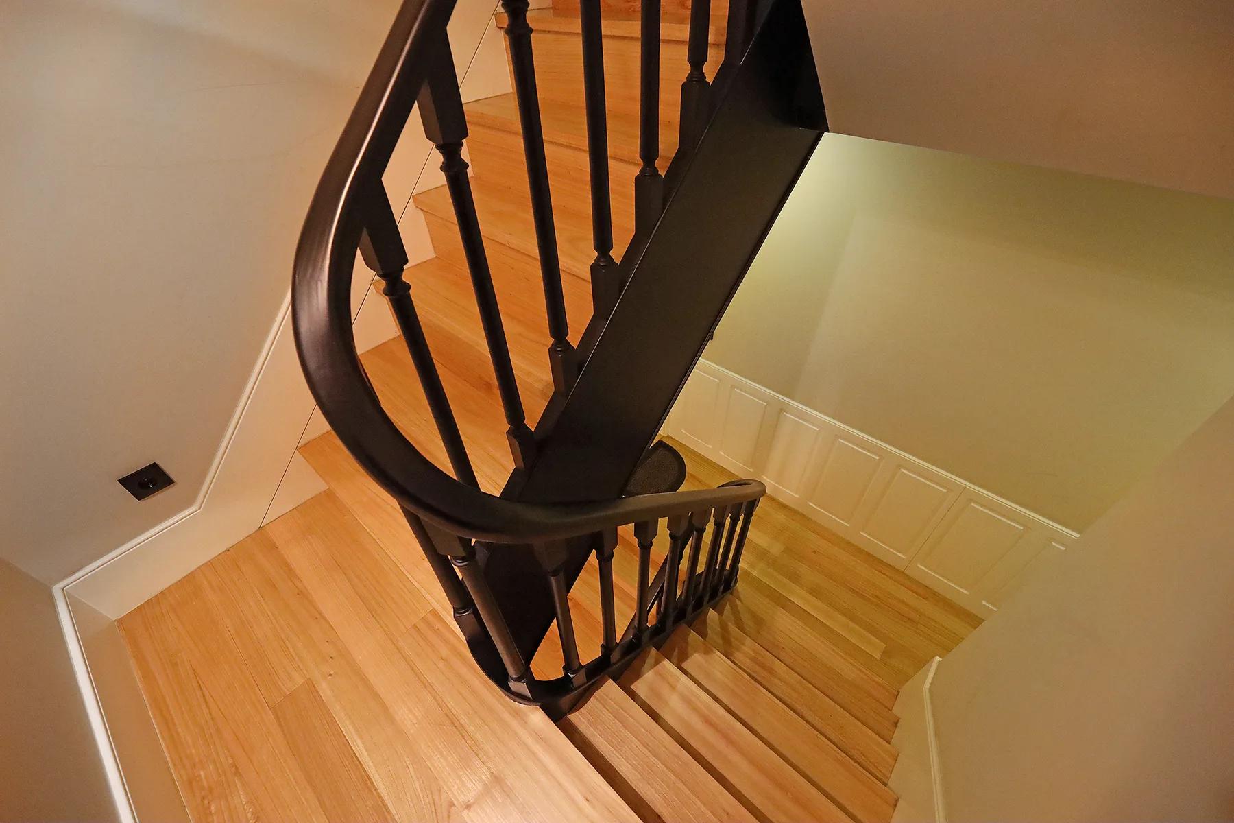 A wooden staircase with dark railings descends through an interior space.