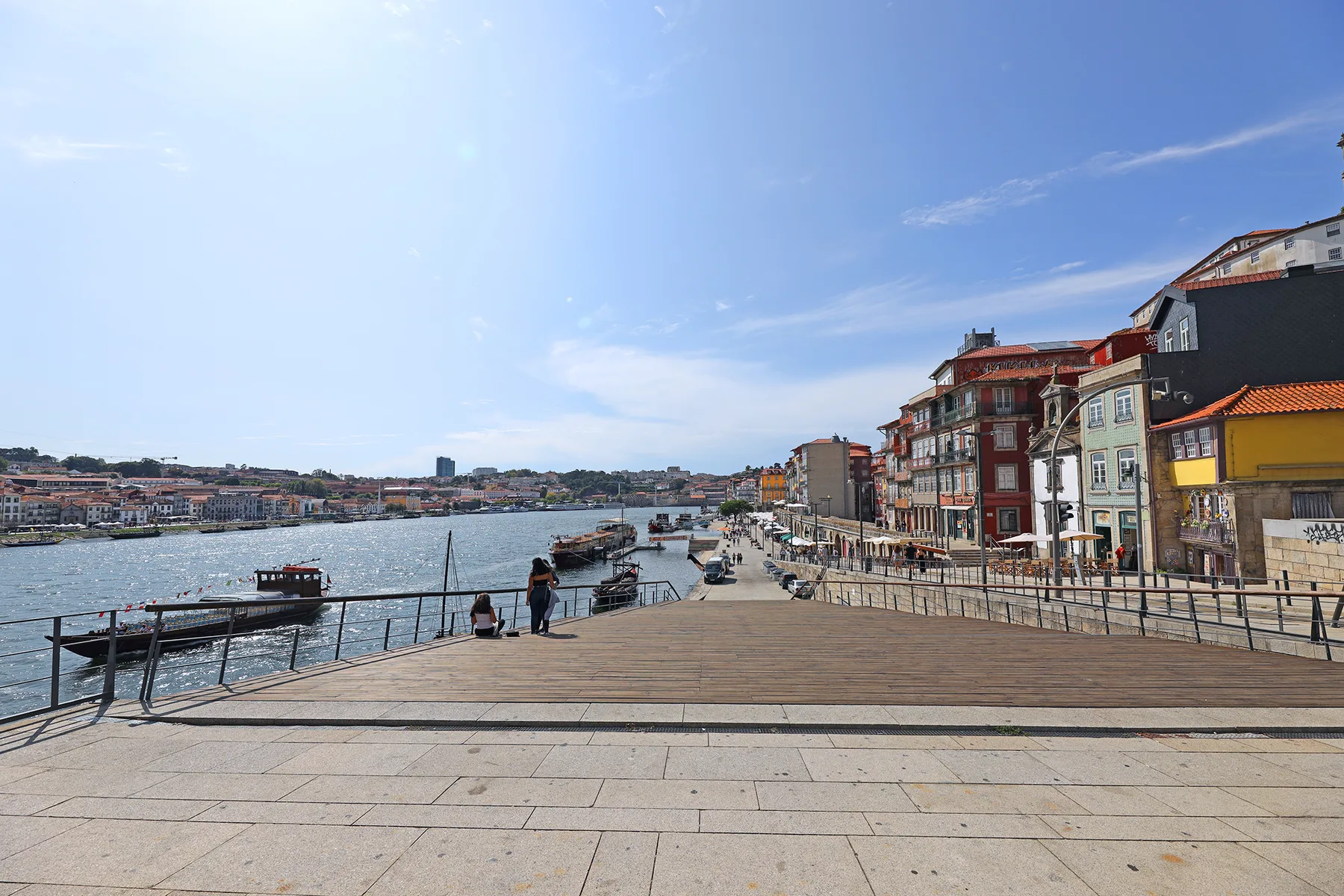A riverside promenade with waterfront buildings and boats along the river.