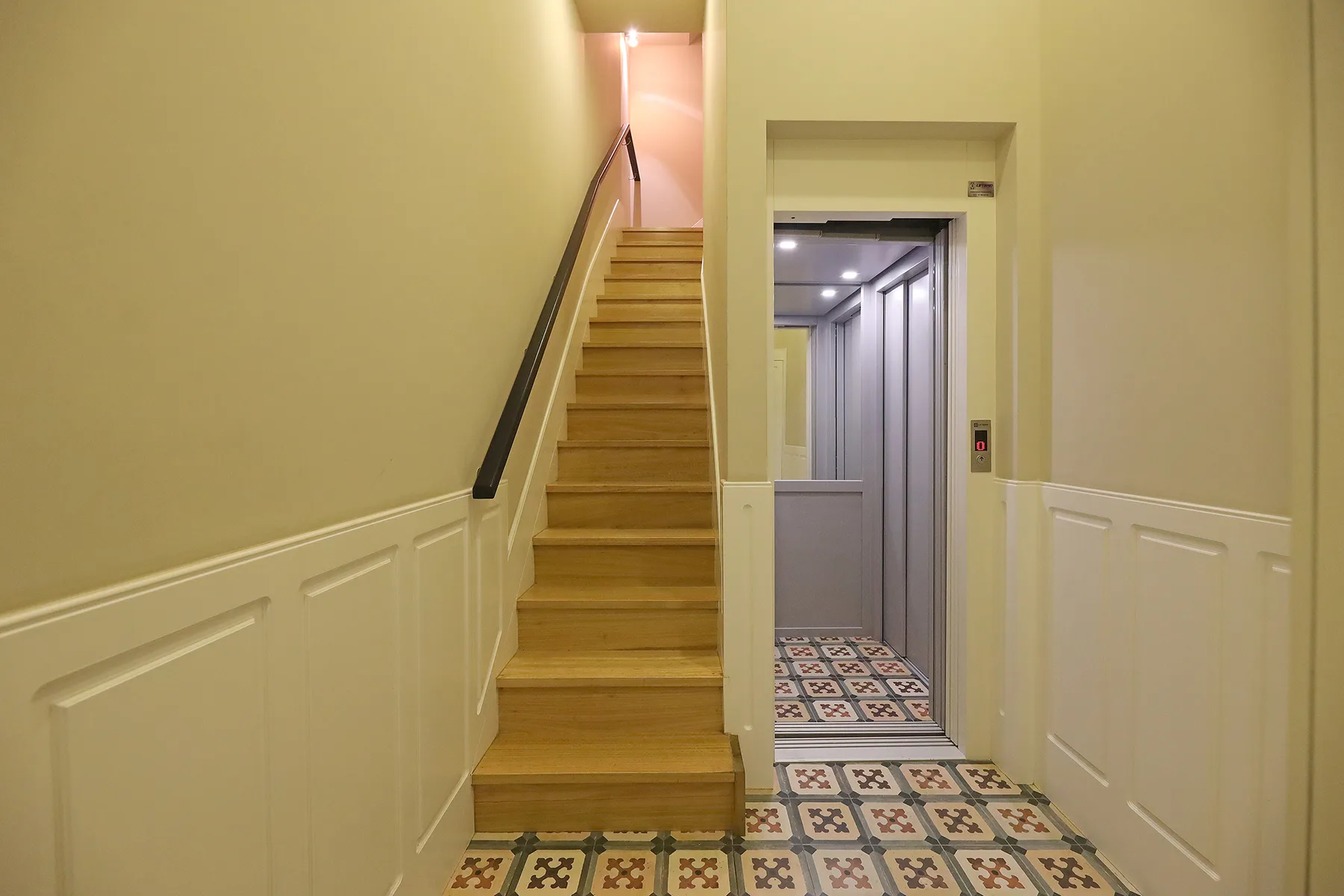 A hallway with a staircase beside an open elevator.