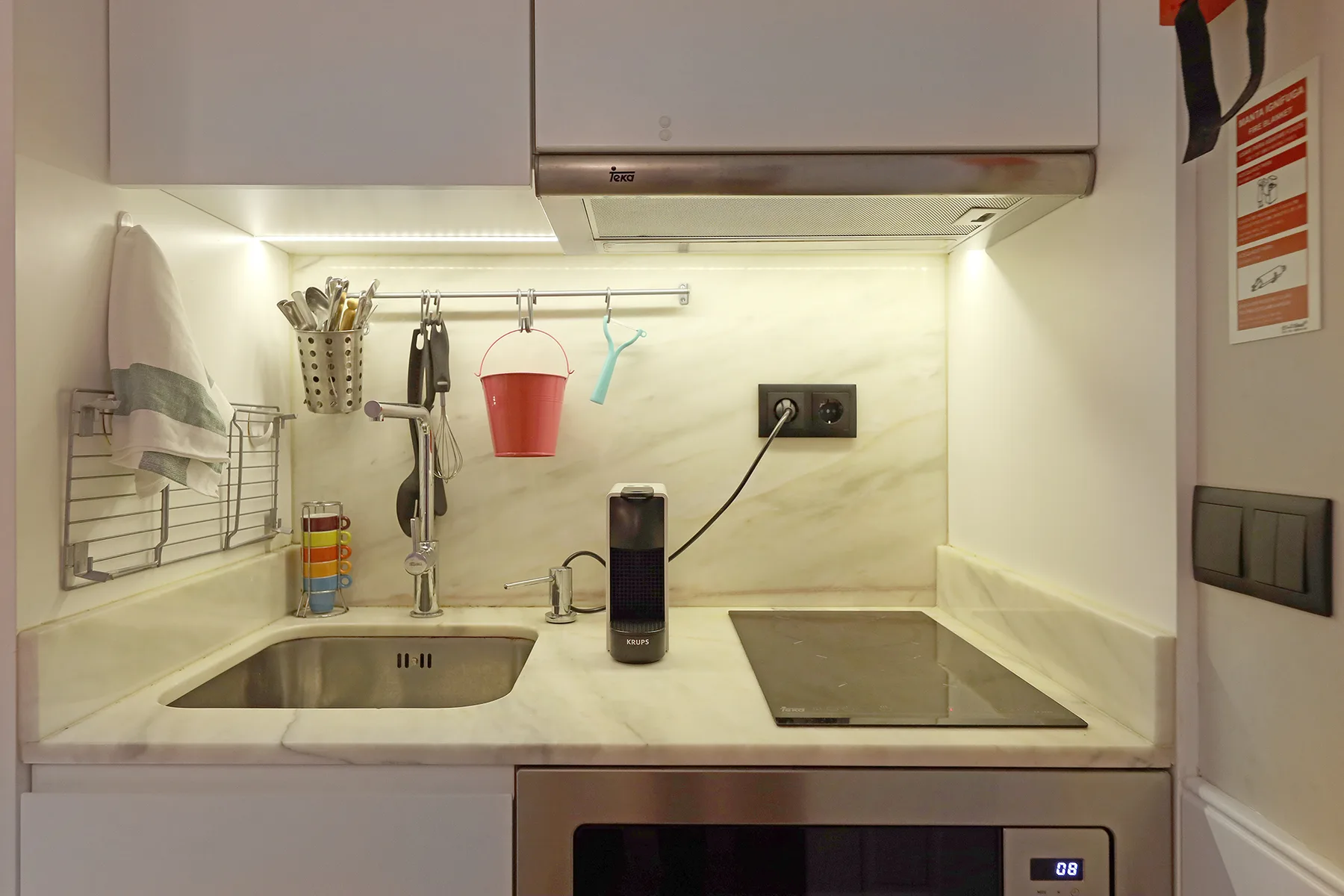 A compact kitchen with a sink, cooktop, and overhead cabinets.