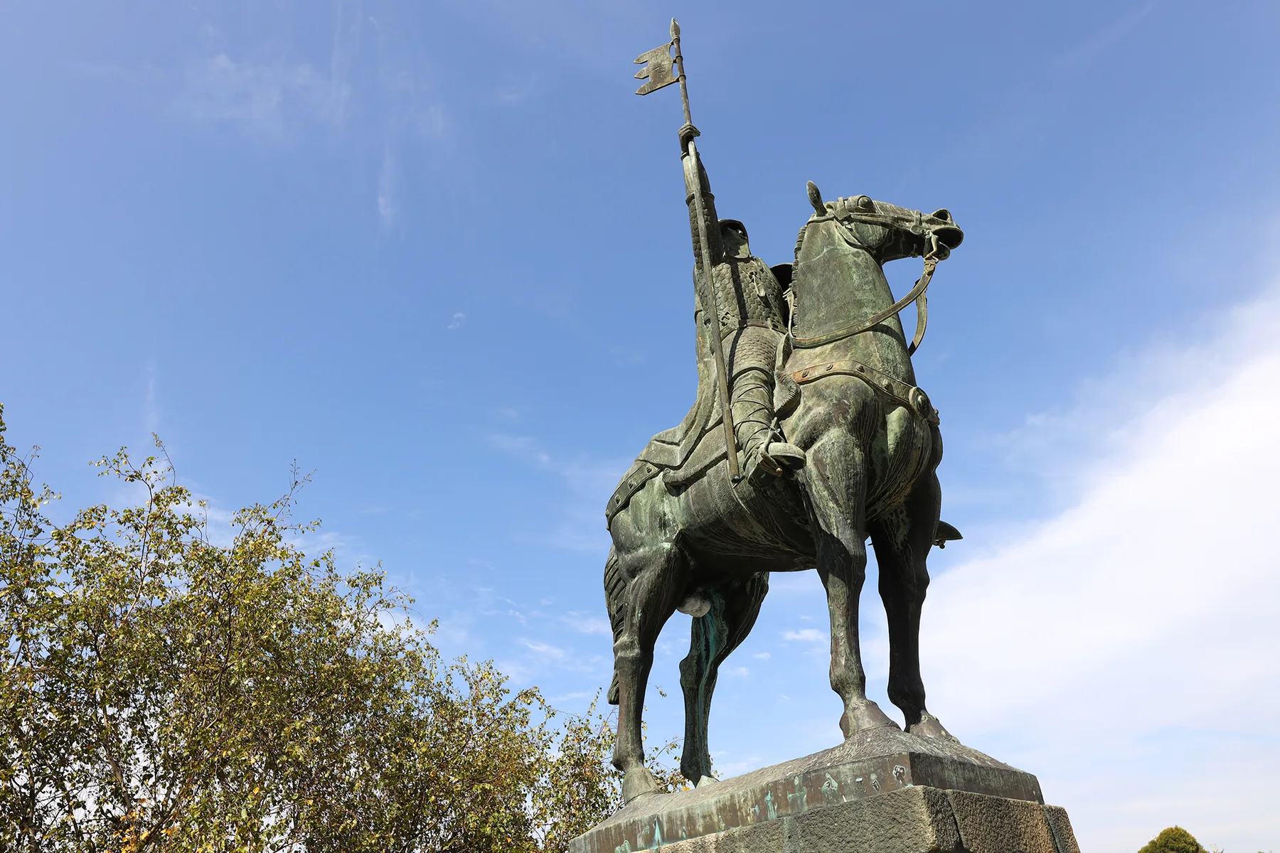 An equestrian statue rises above a stone pedestal against a blue sky.