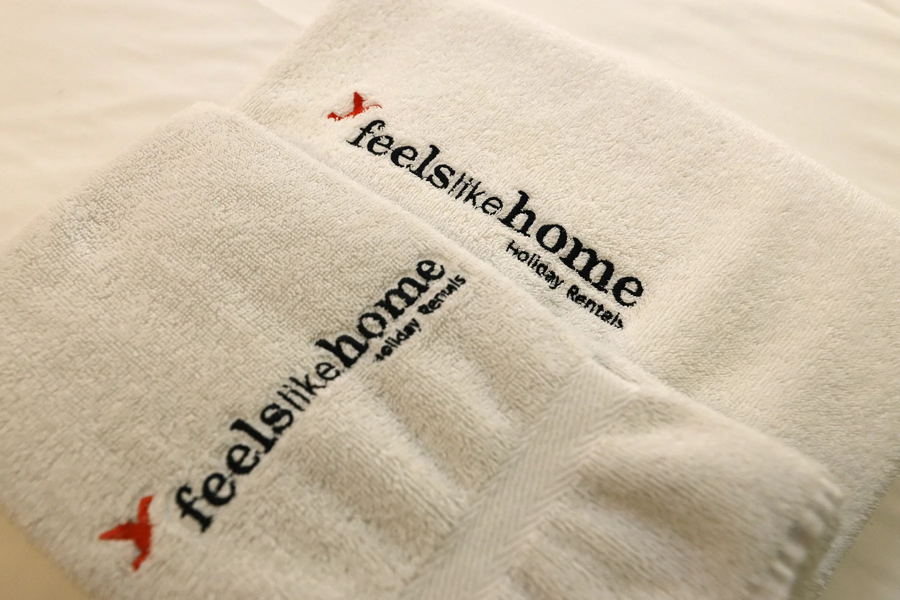Close-up of white towels embroidered with the Feel Like Home logo.