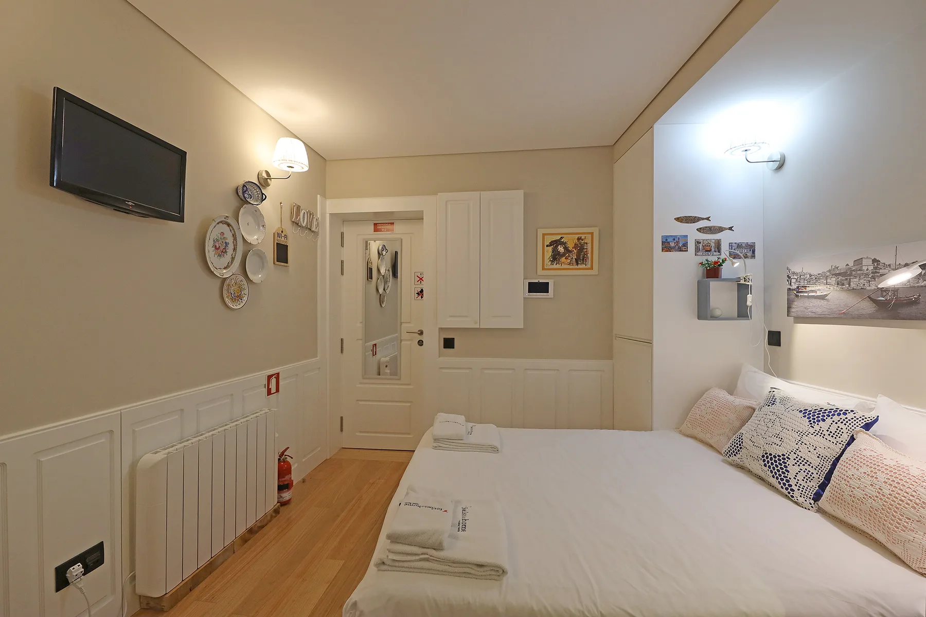 A bedroom with a bed, wall-mounted television, and pale paneled walls.