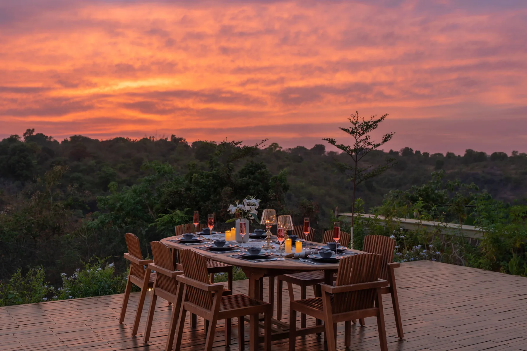 Una mesa de comedor al aire libre con sillas da a un paisaje boscoso al atardecer.