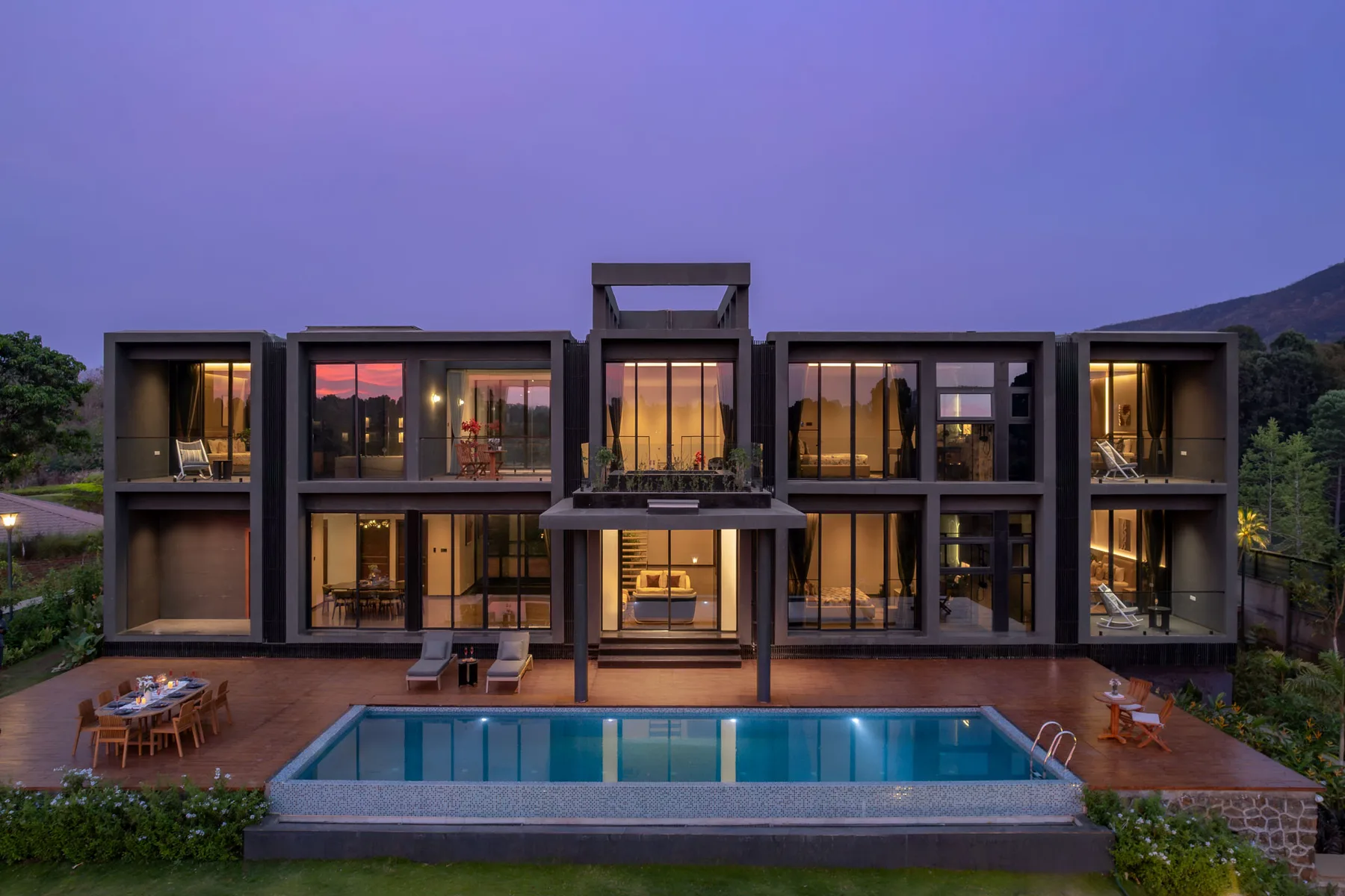 Una casa moderna con grandes ventanales da a una piscina al anochecer.