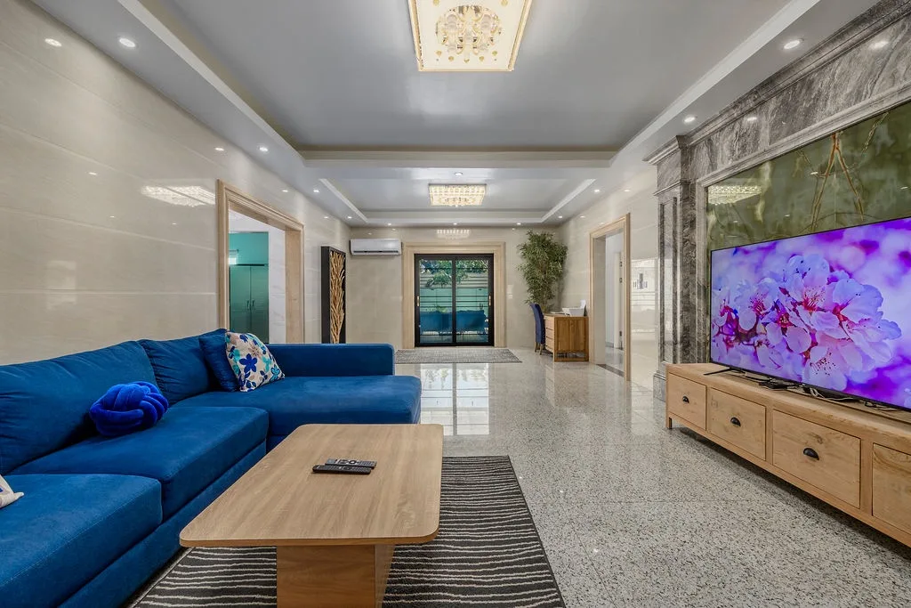 Relax in your spacious living room with plush blue seating, elegant chandeliers, and polished floors that catch the light—a bright and stylish space to unwind after a day of exploring.