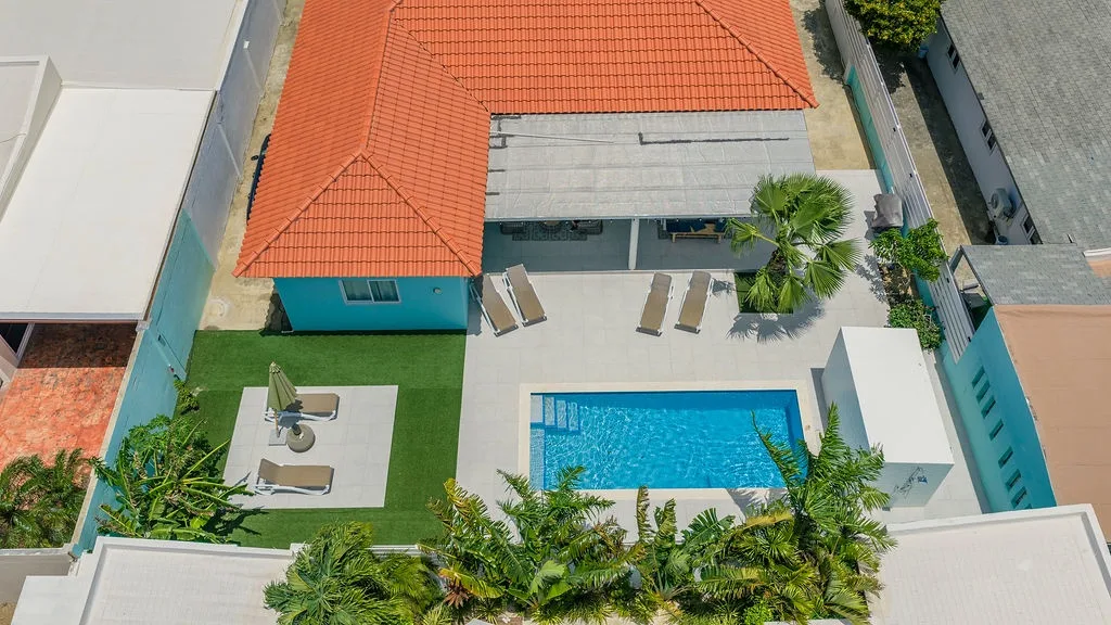 The property offers a private pool and sunny terrace, framed by lush palms and tropical greenery within secure blue walls—an inviting retreat in a peaceful residential area.