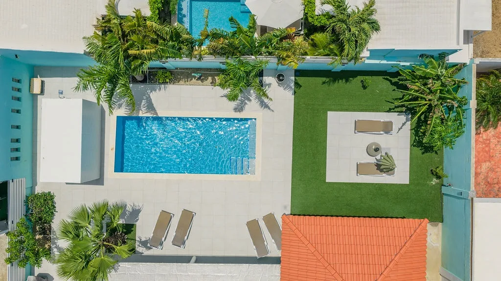 The property showcases a sparkling swimming pool surrounded by lush tropical gardens, sunbeds for lounging, and beautifully landscaped grounds that create your private oasis under the sun.