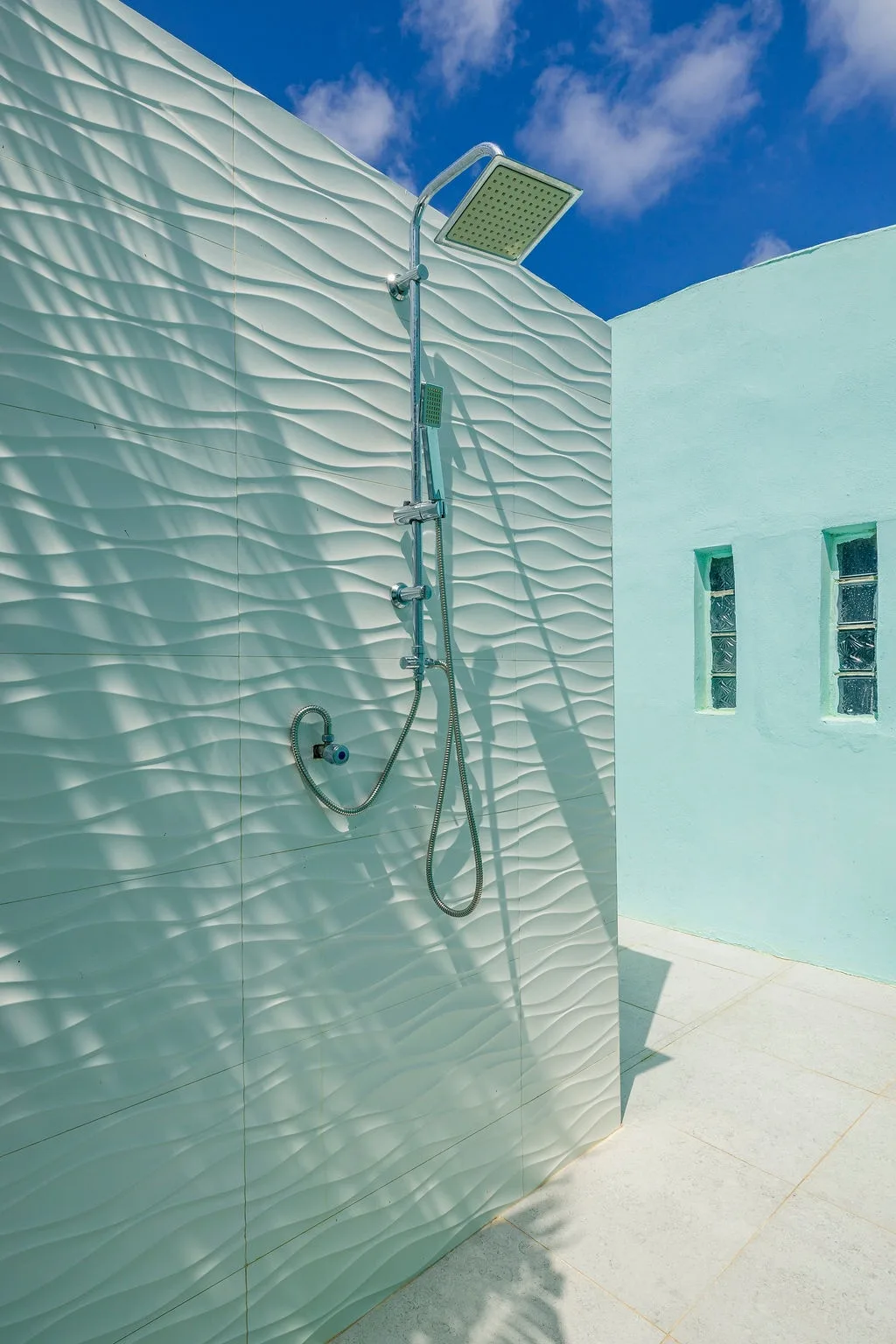 Rinse off under open skies in your private outdoor shower, where textured tile walls meet bright blue above.