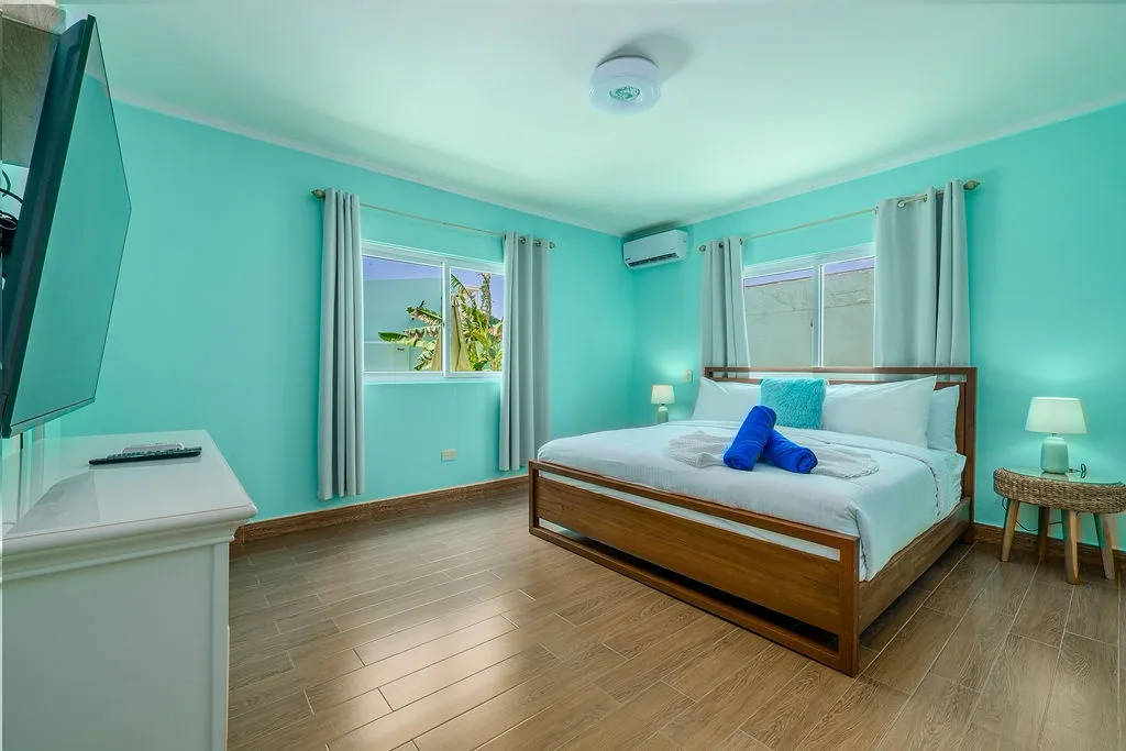Wake up refreshed in your bright bedroom, where tropical turquoise walls surround a cozy bed topped with plush towels—your personal retreat awaits.