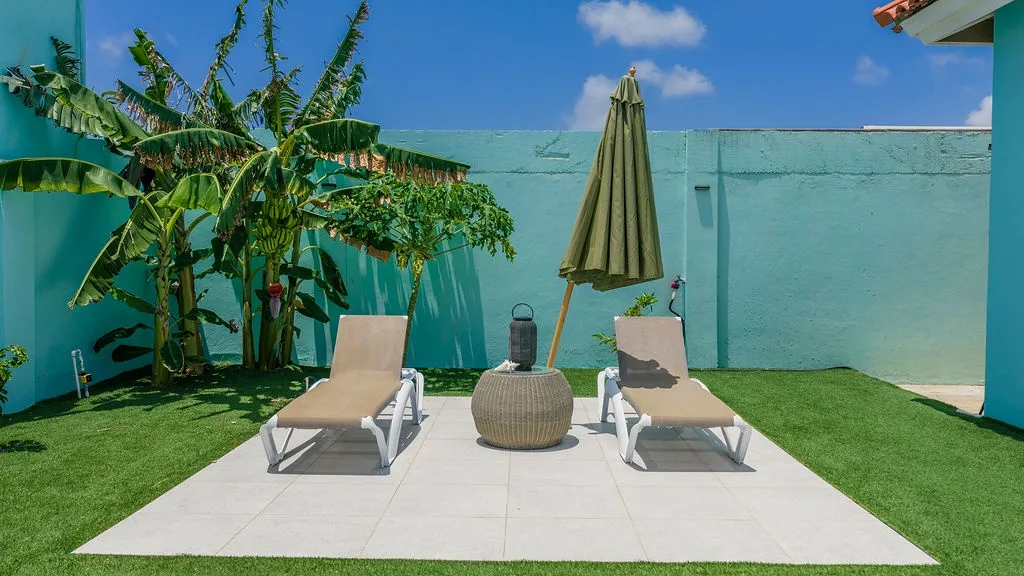 A tranquil outdoor space framed by tropical plants and turquoise walls where you can unwind on sun loungers with refreshing shade nearby.