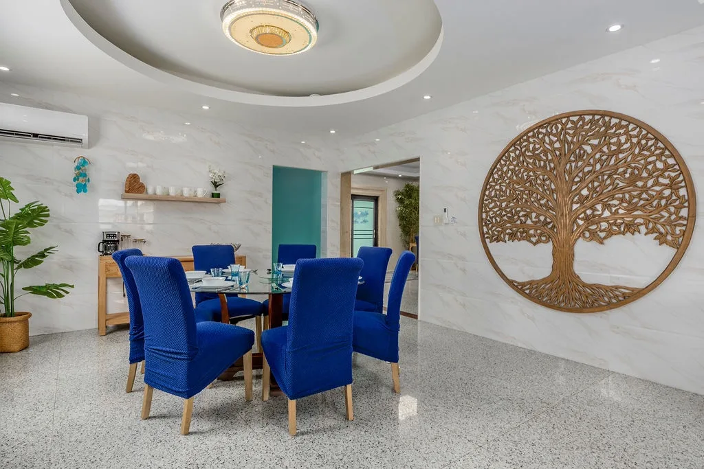Gather around this elegant dining space with striking blue velvet chairs and a statement tree-of-life centerpiece—your perfect setting for shared meals and memorable conversations.