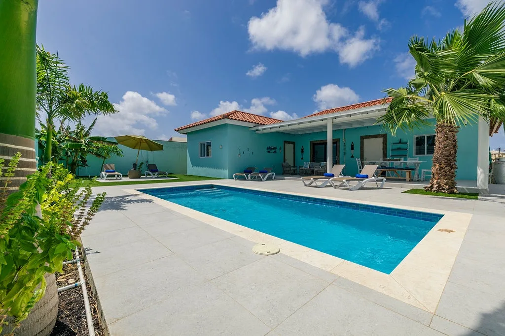 Your private tropical retreat features a sparkling pool surrounded by sun loungers, lush palm trees, and vibrant gardens—perfect for soaking up the island sunshine in complete tranquility.