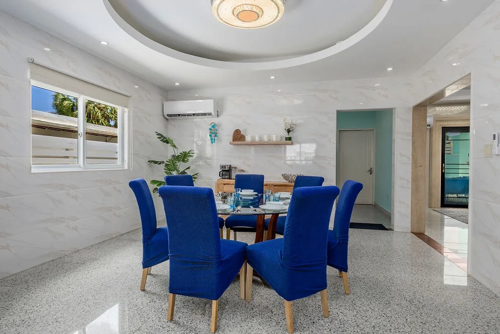 Gather around this elegant dining table with striking blue chairs beneath a sculptural ceiling medallion. The bright, airy space sets the stage for memorable meals together.