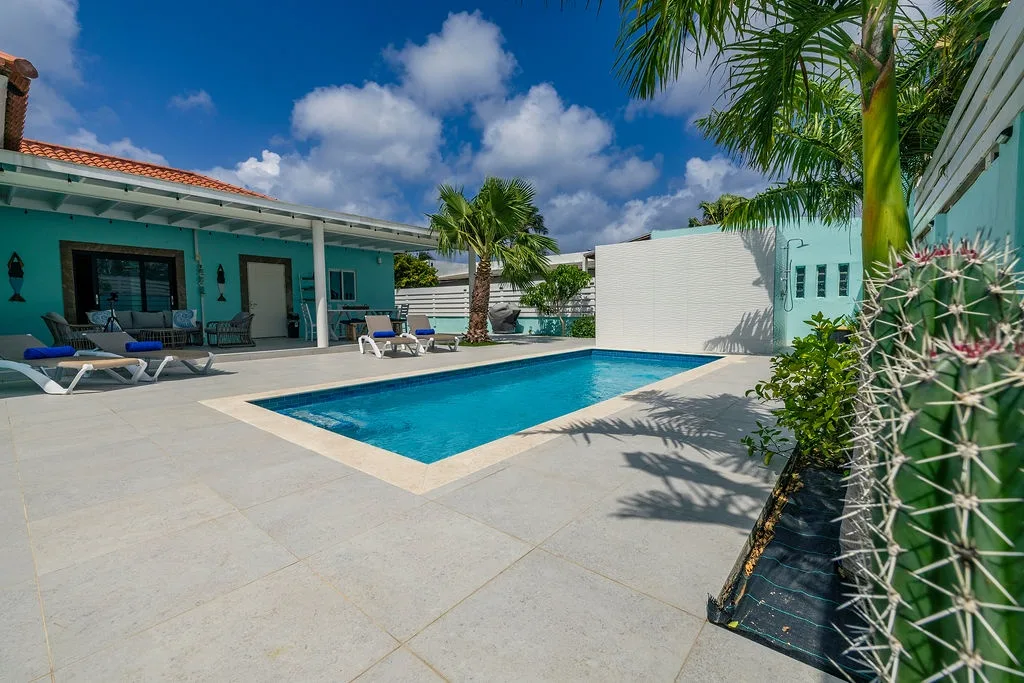 Bright Caribbean architecture and tropical palms frame your private pool—a sun-soaked oasis where you can lounge, swim, and unwind under clear blue skies.