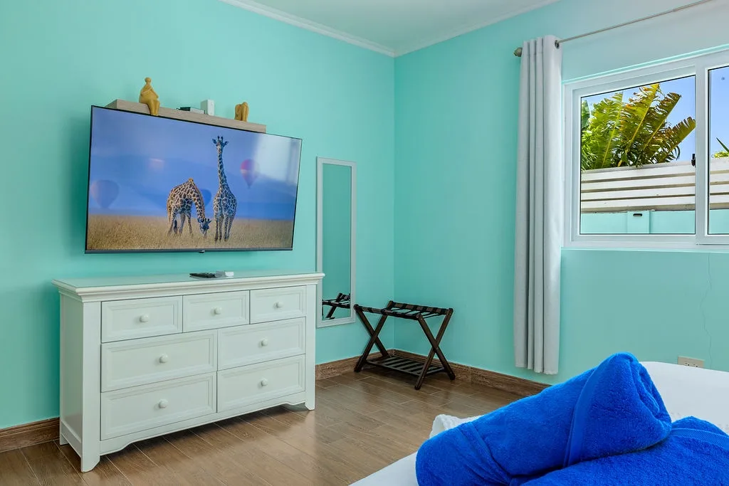 Unwind in your bright tropical bedroom, where fresh turquoise walls and a smart TV create your perfect retreat. Catch a glimpse of swaying palms through the window—paradise awaits.