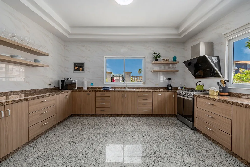 Your spacious kitchen welcomes you with warm wood cabinetry, granite countertops, and natural light streaming through large windows that overlook palm trees and sunny skies.