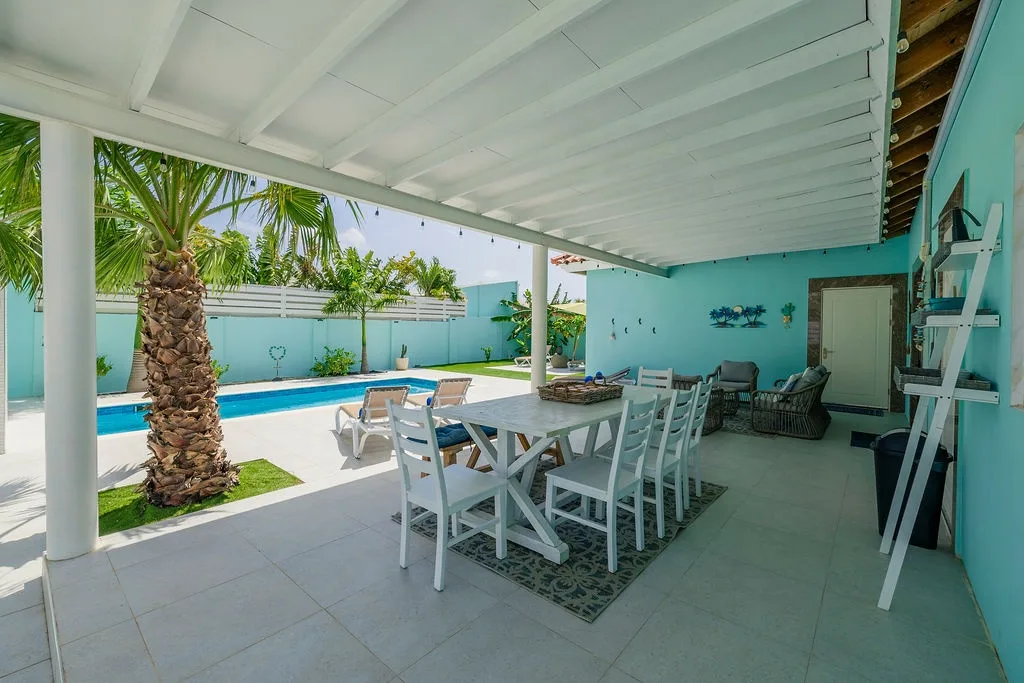 Your private covered patio blends indoor and outdoor living, with a spacious dining table for memorable meals overlooking the sparkling pool and lush tropical palms.