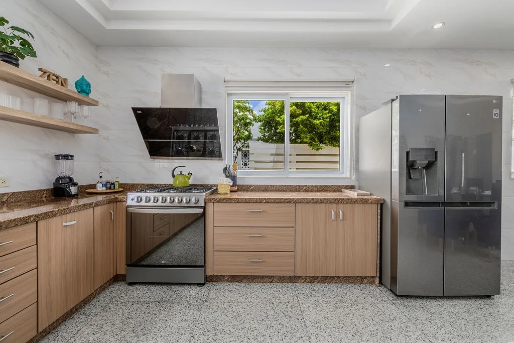 Your modern, fully-equipped kitchen invites you to prepare meals in comfort, with granite countertops, warm wood cabinetry, and a bright window framing leafy garden views—perfect for morning coffee.