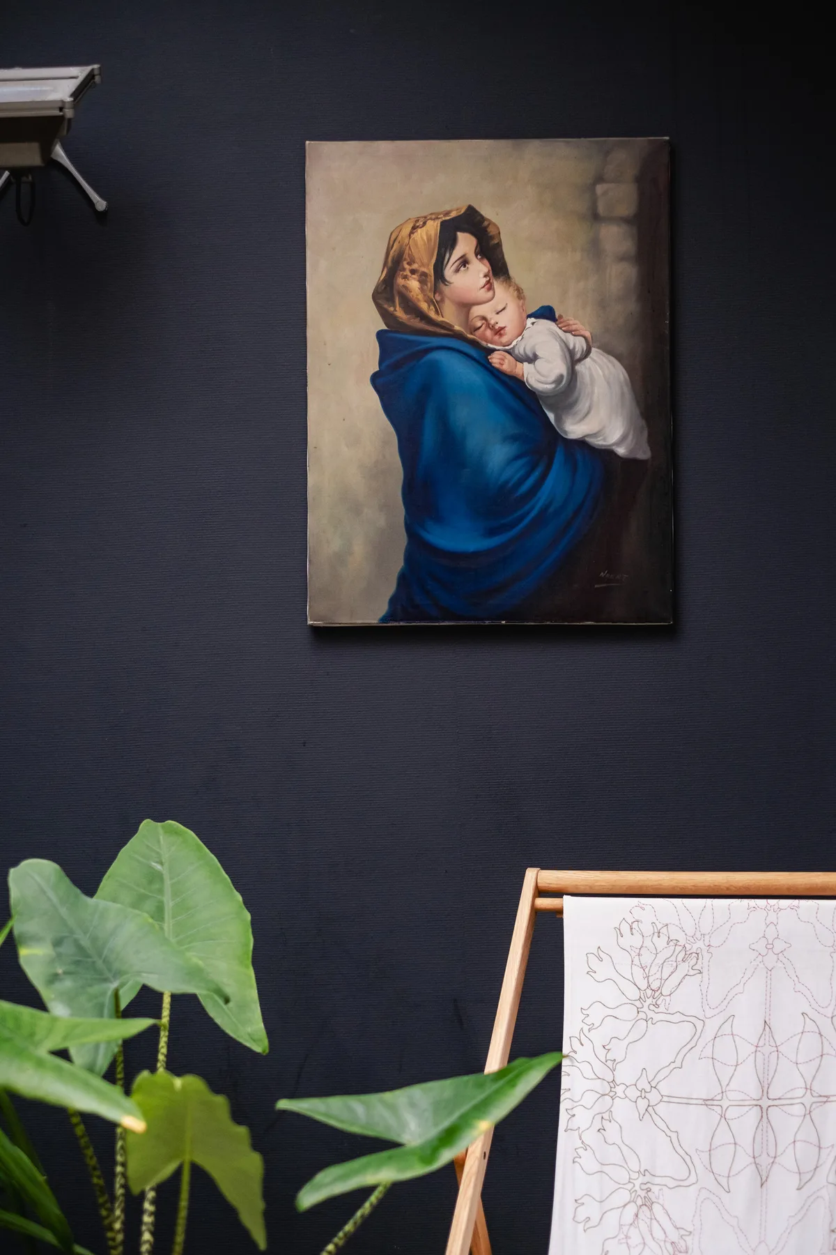 Una pintura enmarcada de una mujer con un niño cuelga de una pared oscura.
