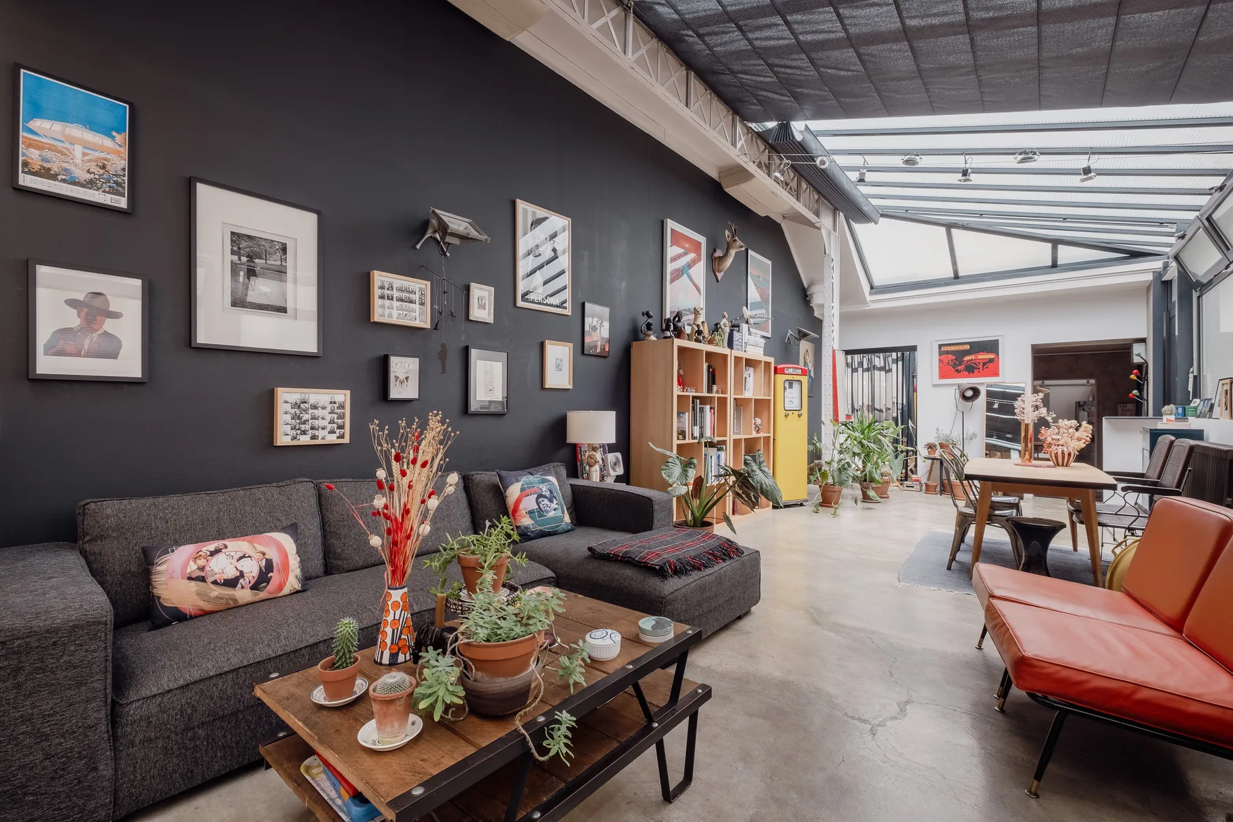 A living room with dark seating, a coffee table, and plants beneath a skylight.