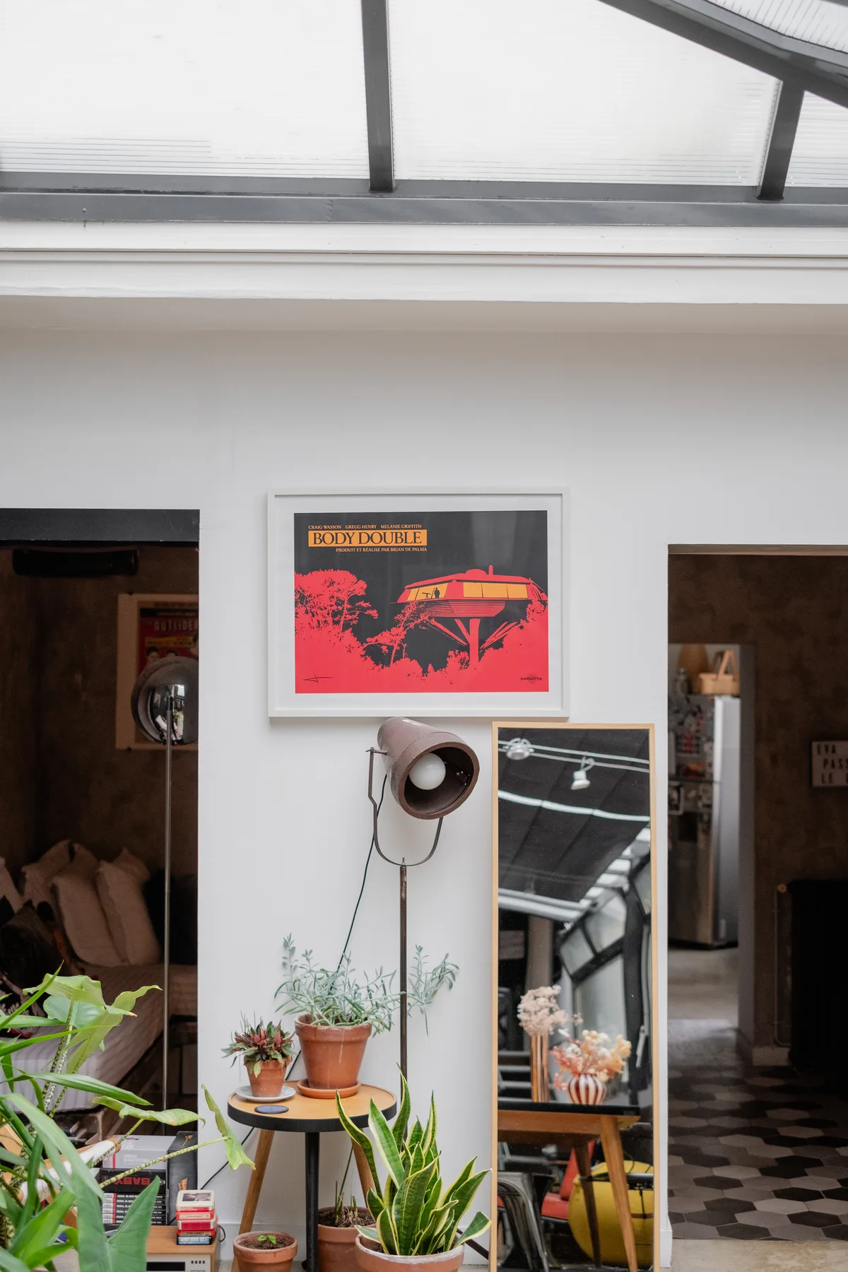 A bright interior with a framed print, leaning mirror, potted plants, and skylight.