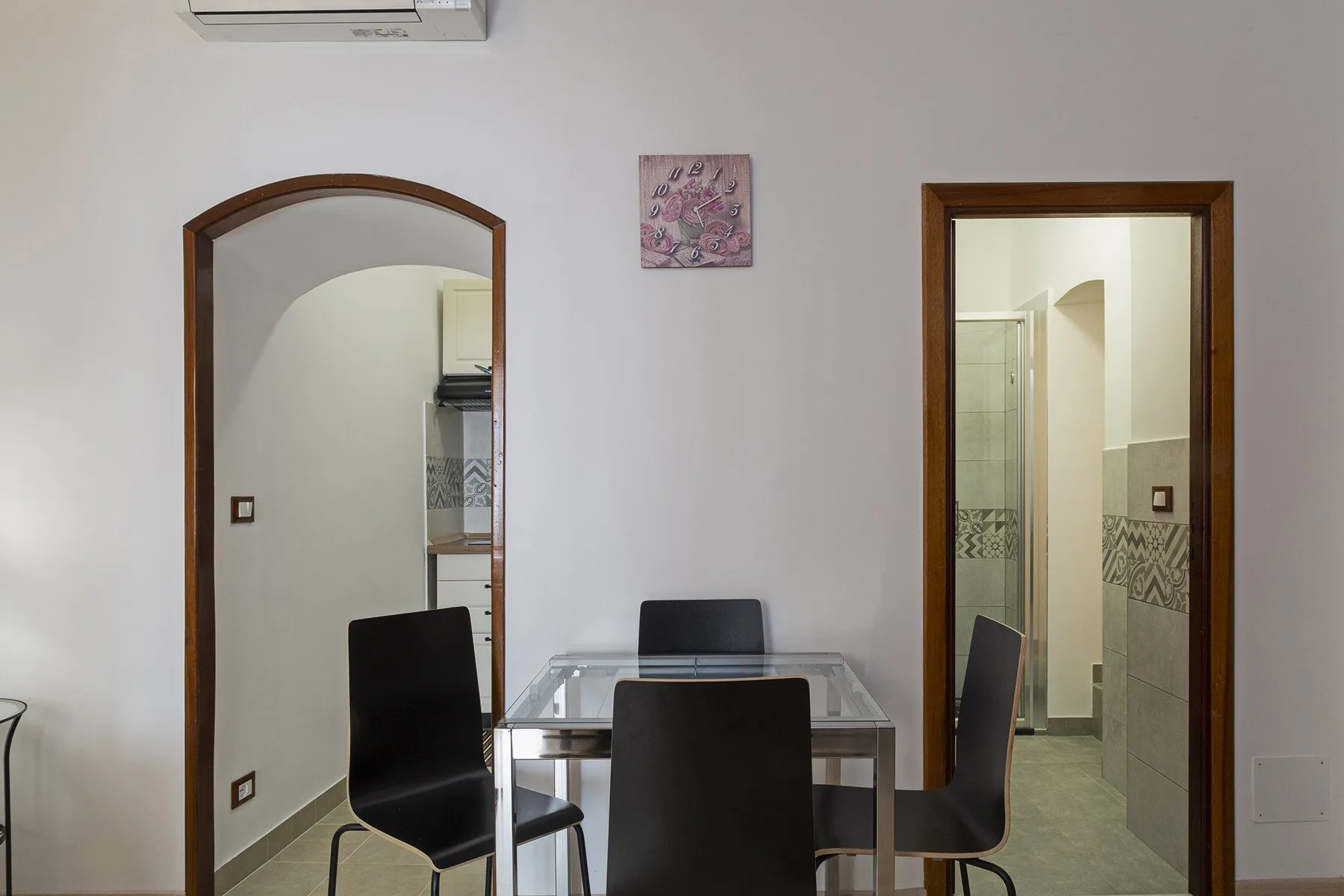 Comedor con una mesa de vidrio y asientos oscuros junto a una puerta abierta.