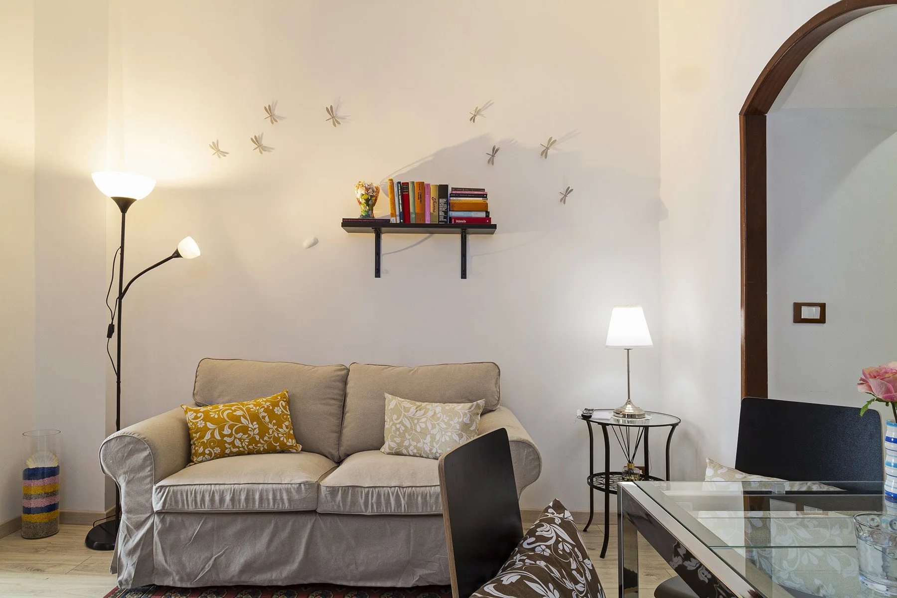 A living room with a sofa, floor lamp, and small wall shelf.