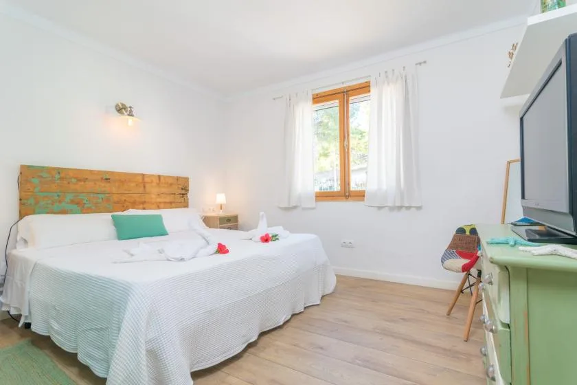 A bright bedroom with a neatly made bed and a window with white curtains.