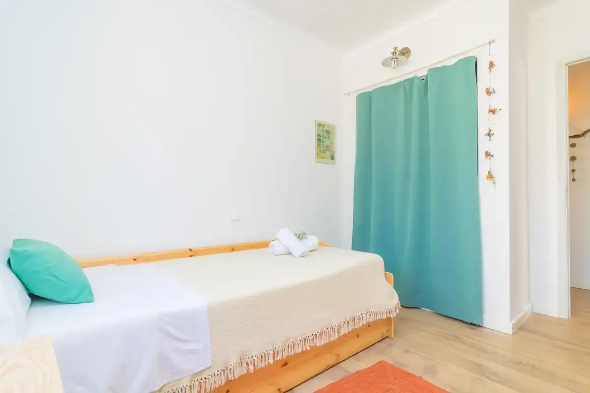 A bedroom with a single bed, turquoise curtains, and light wood flooring.