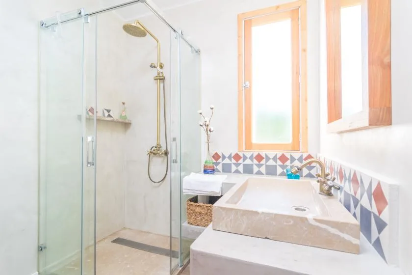 A bright bathroom with a glass shower, bathtub, and patterned tile accents.