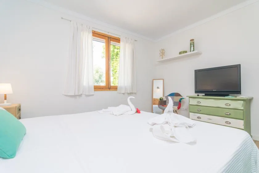 A bright bedroom with a neatly made bed and a television on a dresser.