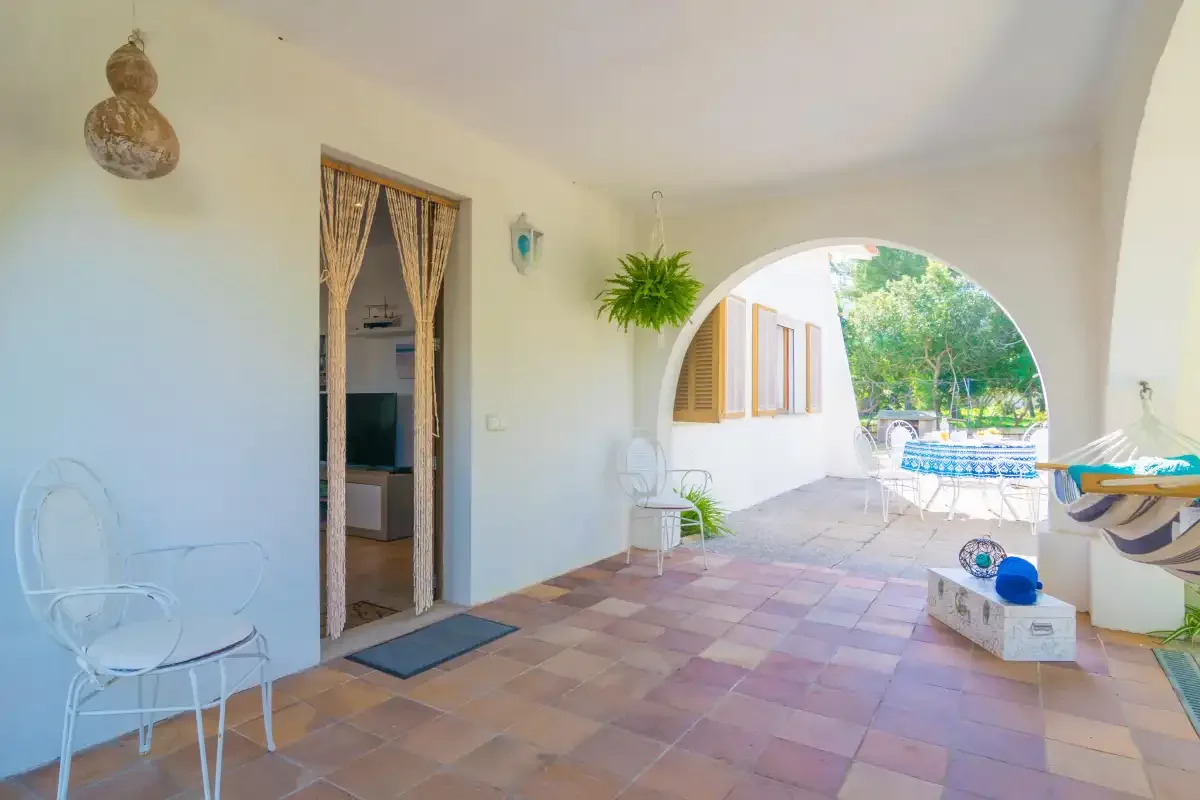 A tiled patio with an arched opening, outdoor seating, and greenery.