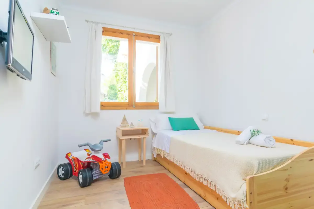 A bright bedroom with a wooden bed, bedside table, and toy truck.