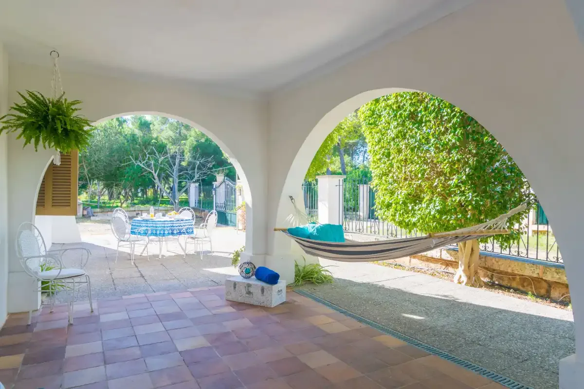 A covered patio with arched openings overlooks a garden and pool.