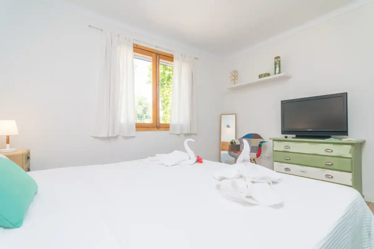 A bright bedroom with a large bed and a television on a dresser.