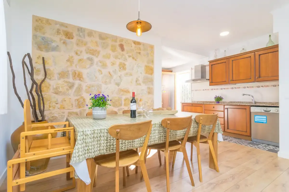 A dining area with a table and wooden seating beside a kitchen with wooden cabinets.