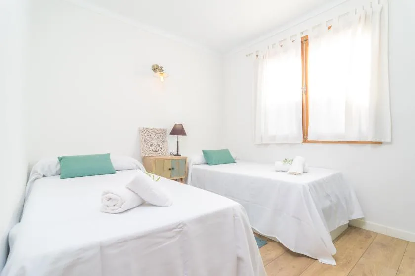A bright bedroom with two beds dressed in white beneath a curtained window.