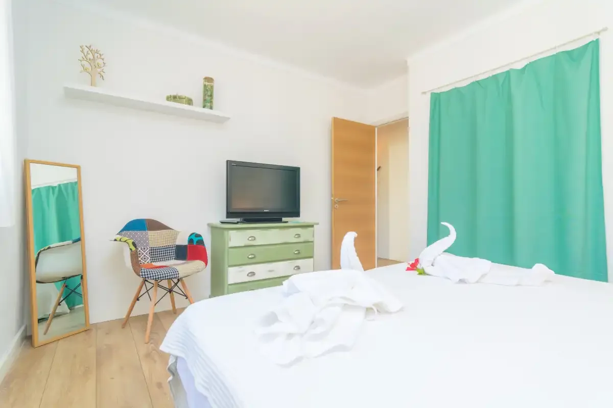 A bright bedroom with a bed, green curtains, and a television on a dresser.
