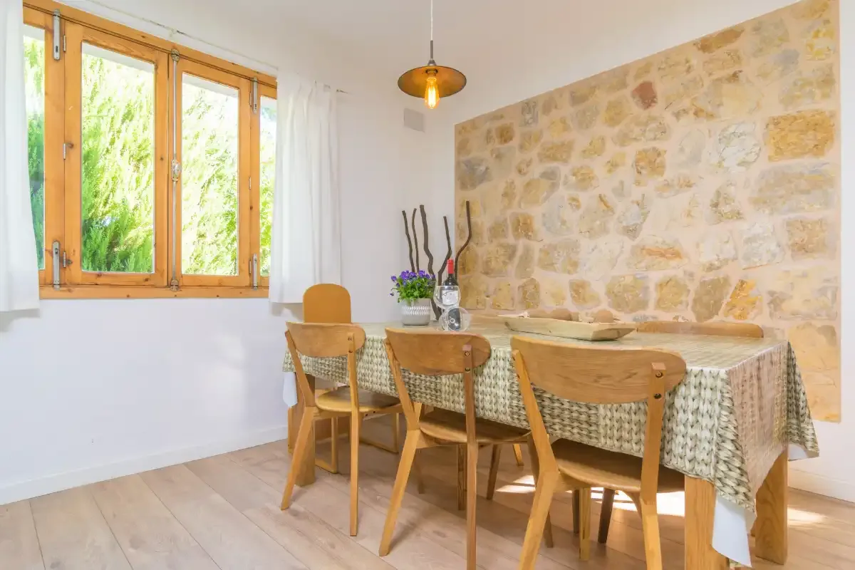 A dining area with a wooden table and chairs beside a stone wall.