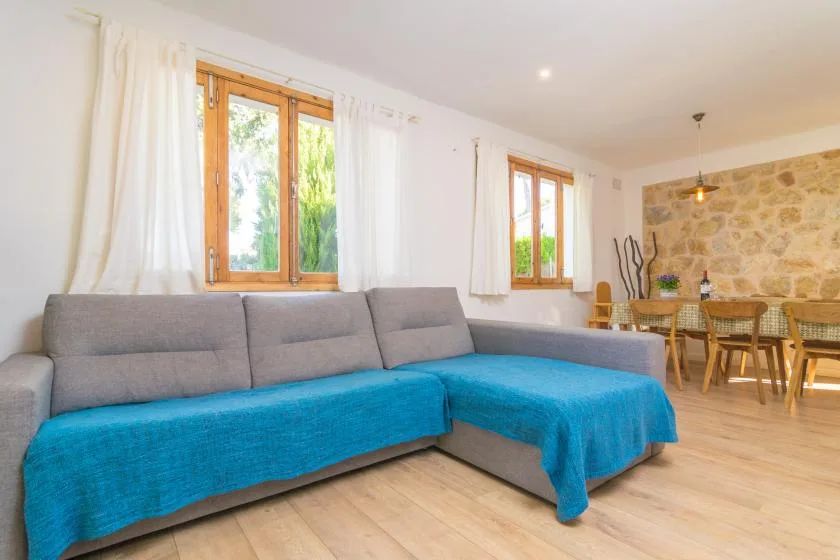 A bright living and dining area with a gray sectional and turquoise covers.