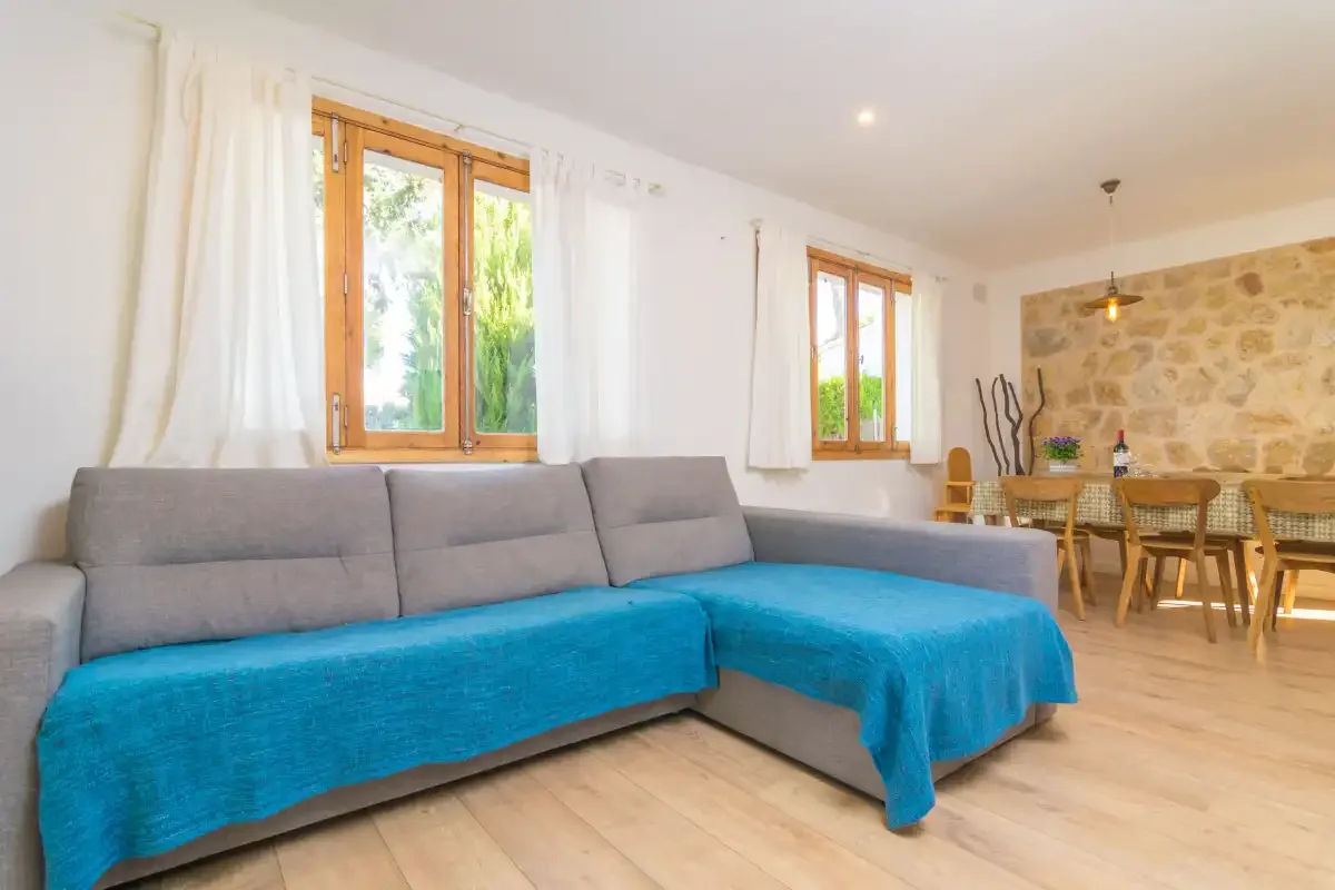 A bright living room with gray seating and a blue cover beside the dining area.