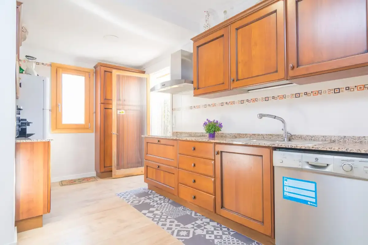 A bright kitchen with wooden cabinets, a countertop, and a patterned floor runner.