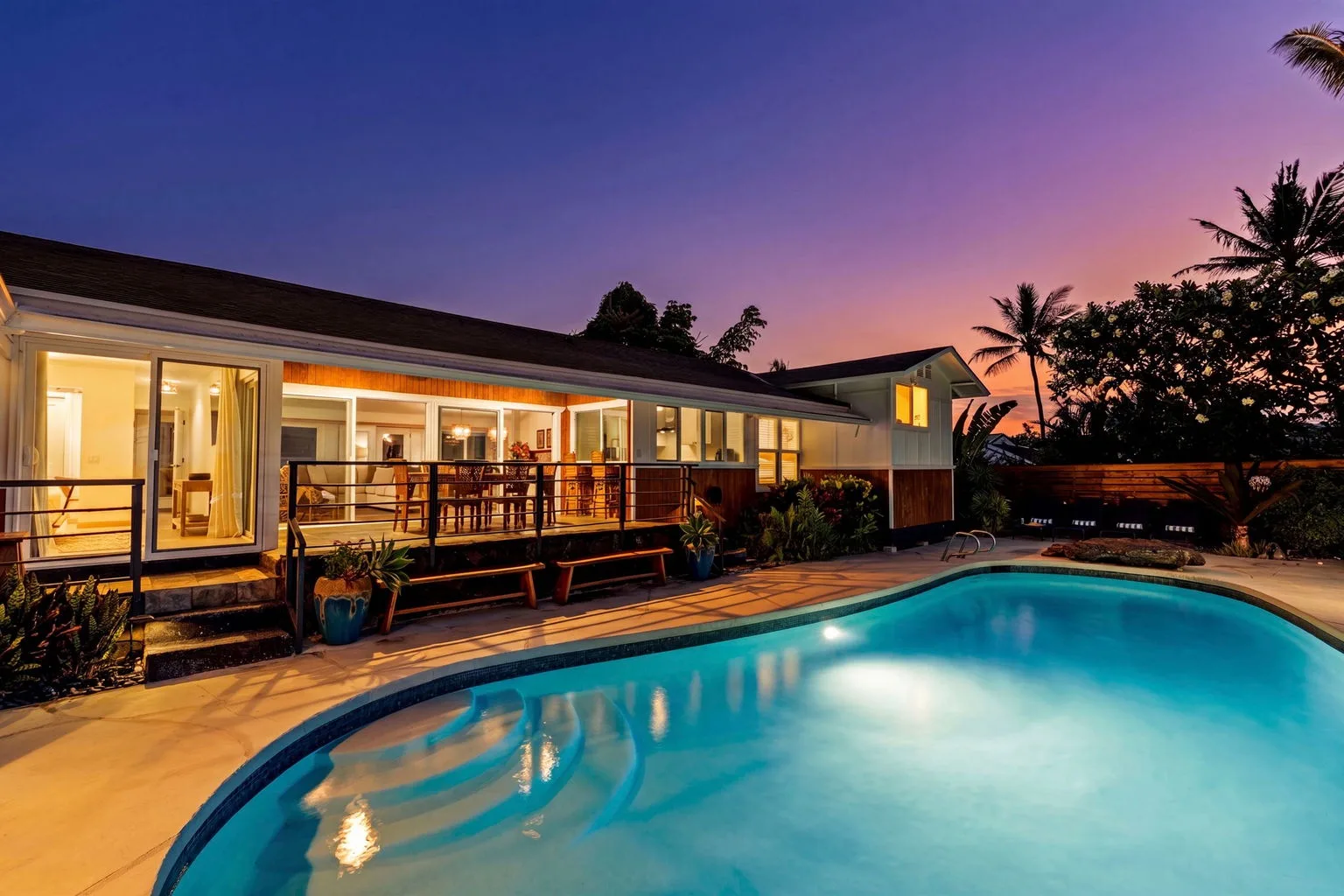 A swimming pool beside a modern house glows beneath the sunset sky.