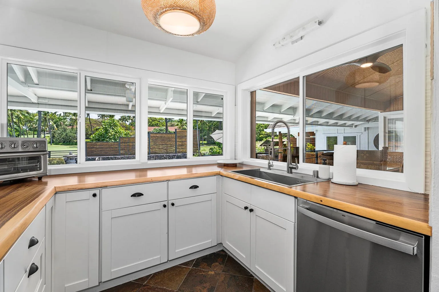 A bright kitchen with white cabinets, wooden countertops, and large windows.