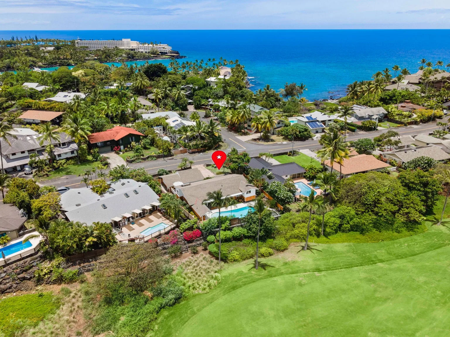 Aerial view of a coastal neighborhood with homes, greenery, and the ocean.